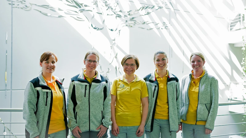Gruppe von Mitarbeitern im Qualitätsmanagement in einheitlicher Arbeitskleidung vor einer modernen Büroeinrichtung